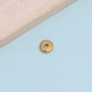Macro detail of golden stainless steel spacer bead for DIY jewelry making on light blue surface