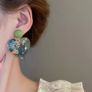 Detail view of heart-shaped earrings featuring tropical monstera and floral print