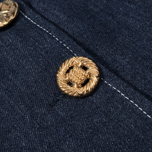 Détail du tissu denim bleu foncé avec bouton vintage doré et surpiqûres blanches