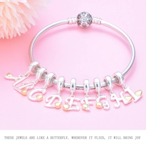 Silver bead bracelet featuring gold heart alphabet charms from A to I on pink background