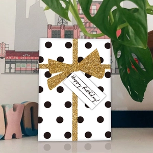 Close-up of birthday card with black polka dots, gold glitter bow, and Happy Birthday tag