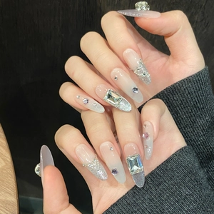Close-up of almond-shaped press-on nails with silver glitter and large crystal rhinestones