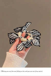 Detail of checkered bow scrunchie with pearls held by hand over beige knit fabric