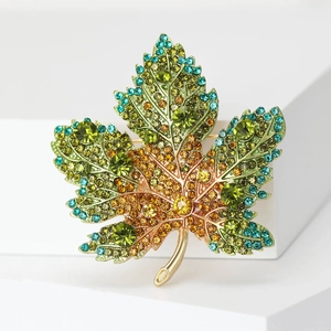 Elegant maple leaf brooch with vibrant green, blue, and yellow crystals on metal base