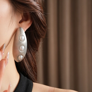 Gros plan d'une boucle d'oreille ovale en argent brossé avec trois perles sur un mannequin