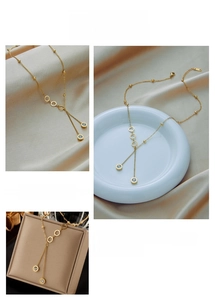 Macro detail of golden Y-shaped tassel necklace with Roman numeral engraved rings