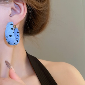 Close-up of a light blue fabric wrapped hoop earring with black polka dots on model