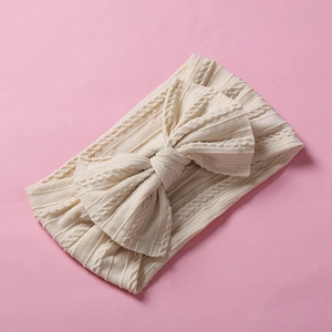Detailed view of cream jacquard knitted baby headband with large bow on pink background