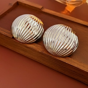 Close-up of silver-tone round striped metal earrings on a rustic dark wood tray