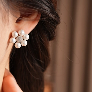 Close-up of elegant pearl flower earrings with zircon centers worn by a model