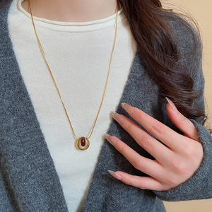 Close-up of gold U-shaped pendant with reddish-brown bead on a chic snake chain necklace