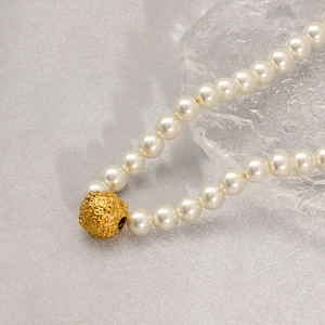 Elegant handmade white shell pearl necklace with a textured gold bead on grey fabric