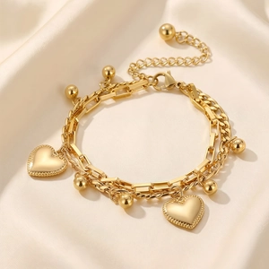 Detailed close-up of golden multi-layer chain bracelet with heart pendant on silk