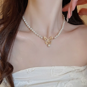 Collier ras du cou en perles avec pendentif papillon doré porté par un modèle