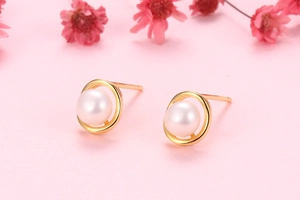 Detail of round freshwater pearl earring with golden circular hollow frame on pink background