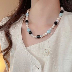 Detail of beaded necklace with light blue, black, and pearl beads on a model's neck