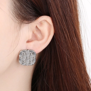 Macro detail of square silver stud earring with woven texture shown on a model's ear