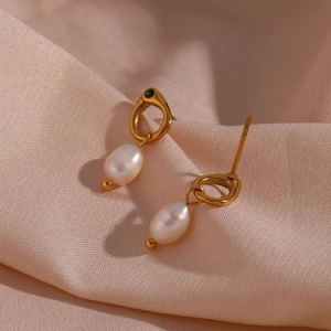 Macro shot of gold earrings with baroque pearls and green gemstones on beige silk