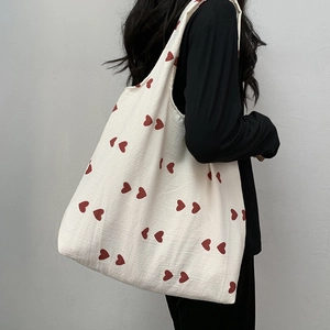 Detail of red heart prints on beige canvas tote bag shown on model's shoulder