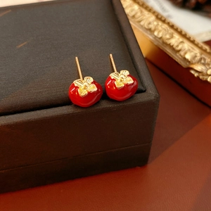 Detailed close-up of persimmon shaped earrings with red glaze and golden leaf accents