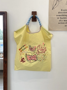 Detailed embroidery on a yellow canvas tote bag with colorful heart patterns and blue rope handle