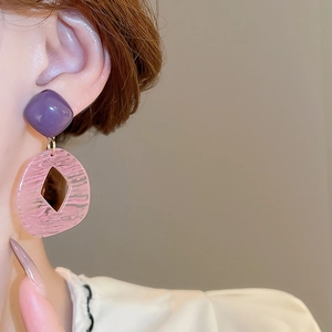 Close-up of geometric resin earrings with purple square stud and pink diamond cutout pendant