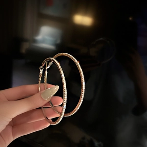 Detail shot of large gold-tone hoop earrings with sparkling crystal pavé held in hand