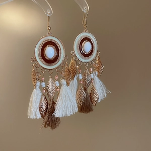 Detail of bohemian gold earrings with white and brown tassels and golden leaf charms