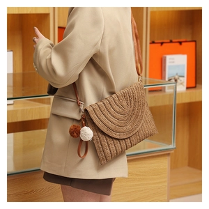 Detail of hand-woven straw crossbody bag with leather strap and decorative pom pom charms