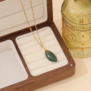 Detail eines grünen tropfenförmigen Edelsteins an einer goldenen Edelstahlkette in Holzbox