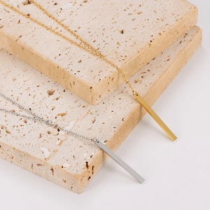 Minimalist stainless steel bar pendant necklaces in gold and silver on beige stone
