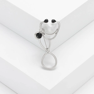 Silver stethoscope brooch with a round black gemstone on a minimalist geometric display
