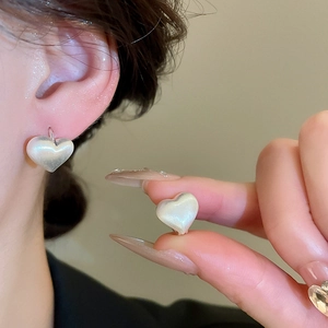 Macro detail of elegant heart-shaped pearl earrings worn on a model's ear