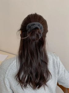 Détail d'un chouchou en maille gris foncé tenant un chignon sur un fond doux