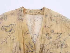Close-up of deep V-neckline with blue floral print on yellow pleated fabric