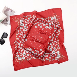 Flat lay of a red silk scarf with white floral patterns and gold chain border detail
