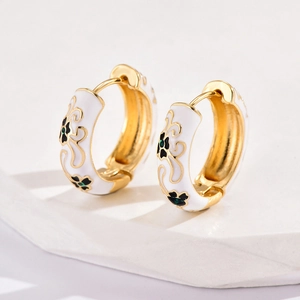 Macro detail of gold-plated hoop earrings with white enamel and black floral patterns