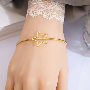 Detail of gold-toned star knot open cuff bracelet worn with elegant lace cuff