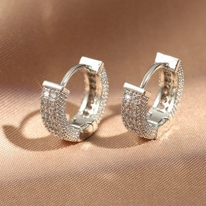 Sparkling silver hoop earrings with full pavé crystals on a silk fabric background