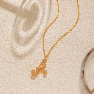 Detail of 18K gold plated necklace with a cursive letter A pendant micro-pave with zircons