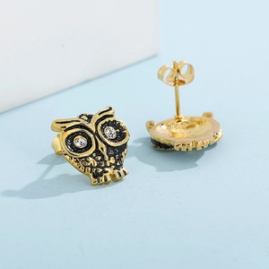 Vue macro de boucles d'oreilles hibou dorées avec cristaux et détails en émail noir