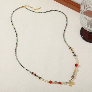 Detail of beaded necklace featuring African turquoise, freshwater pearls, and gold horse charm