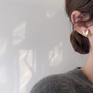 Close-up of gold heart-shaped stud earring with unique hammered texture on model's ear