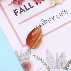 Macro detail of striped orange agate teardrop pendant on a floral decorative card