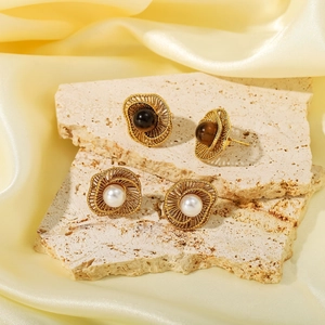 Détail de boucles d'oreilles fleur évidée avec œil de tigre et perle sur travertin