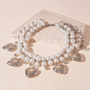 Layered faux pearl and silver heart pendant necklace on minimalist textured stone