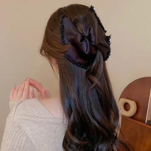 Elegant large black satin bow hair claw clip with lace trim shown on long wavy hair