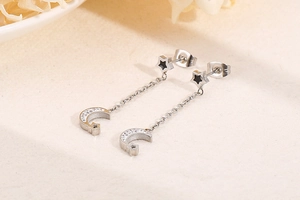 Macro detail of silver tassel earrings featuring black star studs and zircon crescent moon
