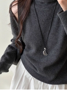 Detailed view of leather cord sweater necklace with silver comb pendant on gray knitwear