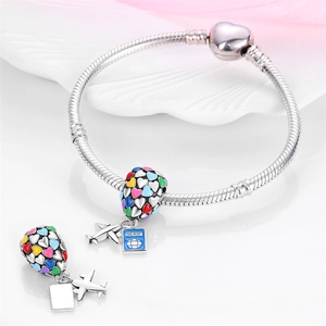 Macro detail of silver snake chain bracelet with enamel hot air balloon and passport charms